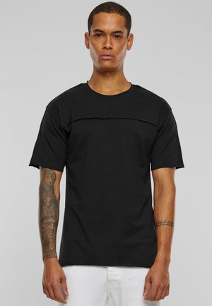 T-shirt noir à col rond et manches courtes, avec un panneau horizontal sur la poitrine. Texture lisse, coupe décontractée, design minimal.