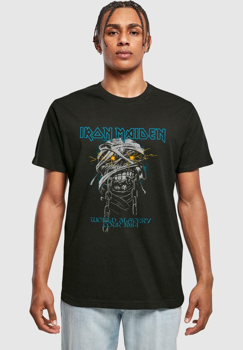 Sort bomulds t-shirt med Iron Maiden grafik, kranium design med kæder, detaljeret udført, klare gule accenter i øjnene, blå tekst.