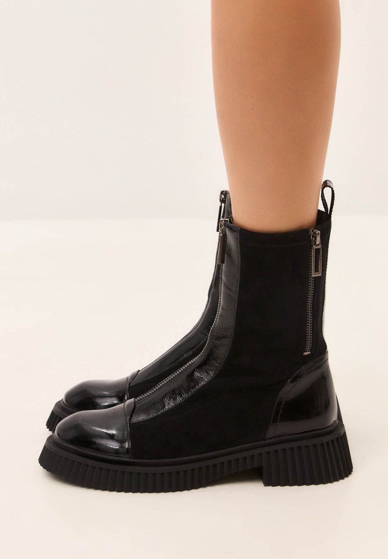 Ghete negre până la gleznă cu un design elegant, realizate din piele lacuită și catifea mată, cu fermoare laterale și talpă groasă din cauciuc zimțat.