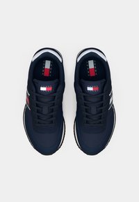 Sneakers blu navy con una superficie liscia, strisce orizzontali bianche e rosse, suola nera a contrasto e etichetta brandizzata sulla linguetta.
