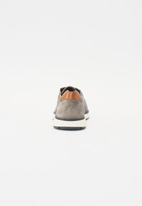 Grå semsket sneakers med en brun lærudal på hælen, hvid mellemsål og sort gummiyttersål, sett fra baksiden.