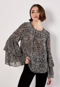 Zwart-witte blouse met een patroon, lange, uitlopende mouwen en een ronde halslijn. Doorzichtige, lichte stof met complexe ontwerpen.