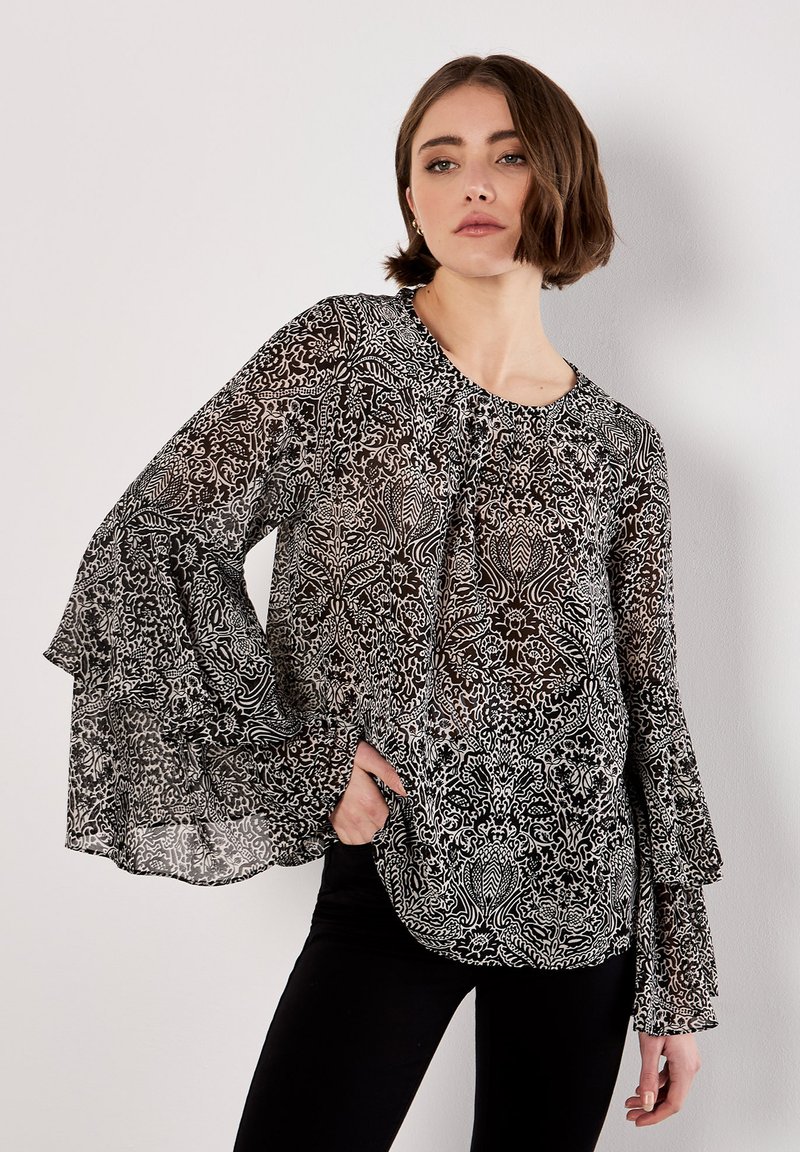 Zwart-witte blouse met een patroon, lange, uitlopende mouwen en een ronde halslijn. Doorzichtige, lichte stof met complexe ontwerpen.
