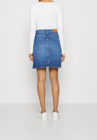 Jeansenkjol med rak skärning, ljusblå färg, med två bakfickor och en märkesläderetikett vid midjan. Bärs med vita sneakers.