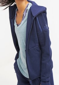 Mörkblå zip hoodie med frontficka, huva och kontrasterande material. Matchas med en ljusblå v-ringad t-shirt.