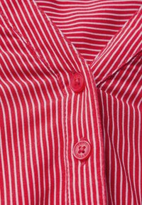 Un tessuto a strisce rosse e bianche presenta un colletto e due bottoni rossi tondi. La texture è liscia con cuciture visibili lungo i bordi.