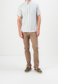 Košile s krátkým rukávem a zapínáním na knoflíky, s světle modrými a bílými vertikálními proužky, spárovaná s béžovými chinos kalhotami a zelenými espadrilkami s hnědými tkaničkami.