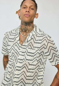 Chemise à manches courtes avec un motif en zigzag noir et blanc, fabriquée dans un matériau léger, dotée d'une coupe décontractée et d'un col ouvert.