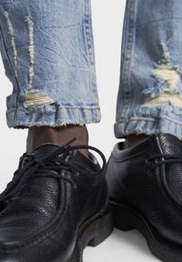 Svarta texturerade läderskor med runda tår och svarta snören, ihopparat med ljusblå slitna jeans som visar fransade fållar och lagningar.