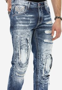 Helle blaue, stark abgewetzte Jeans mit mehreren ausgefransten Löchern, einem verblassten Wasch-Effekt und einem einzigartigen Taschendesign.