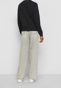 Black sweatshirt with long sleeves and ribbed cuffs, paired with light gray wide-leg jeans and white sneakers. Simple design and relaxed fit.