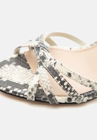 Πέδιλο με λουρίδες σε σχέδιο φίδι μαύρο και λευκό, ανοιχτή μύτη και λεπτά λουράκια που διασταυρώνονται σε μπεζ σόλα.
