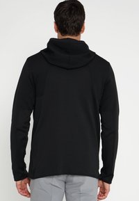 Hoodie noir à manches longues avec une capuche à cordon de serrage. Fabriqué en tissu lisse avec une texture subtile. Présente une coupe décontractée et des coutures minimales.