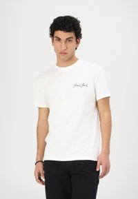White cotton t-shirt with short sleeves, a round neckline, and a small black signature logo on the left chest. Flat texture and classic fit.