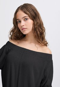 Top nero off-shoulder in tessuto testurizzato e con scollatura ampia. Vestibilità ampia con maniche fluenti, caratterizzato da dettagli plissettati sull'orlo.