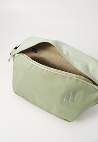 Borsa in tessuto verde con superficie texturizzata, chiusura con zip e interno beige. Presenta un piccolo logo argento sul lato anteriore.