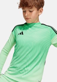 Lange mouwen sportshirt in lichtgroen met een gewaveerd textuurpatroon, zwarte accenten op de schouders, gemaakt van rekbaar, ademend materiaal.