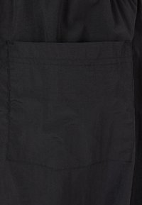 Černá látka s texturovaným povrchem a viditelným detailem kapsy. Design je jednoduchý, zaměřený na funkčnost bez ozdob.