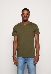Tricou scurt cu maneci verzi măslinii, fabricat din bumbac. Prezintă un guler rotund și o croială lejeră, asortat cu blugi albaștri deschis.