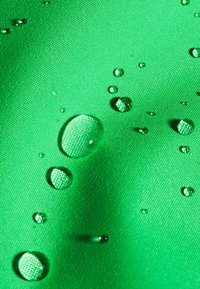 Gocce d'acqua che si raccolgono sulla superficie di un tessuto verde testurizzato, evidenziando la resistenza all'acqua o il materiale impermeabile.