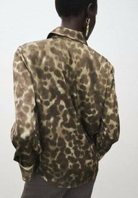Green and brown patterned blouse with a relaxed fit, long sleeves, and a classic collar, made from a silky material.