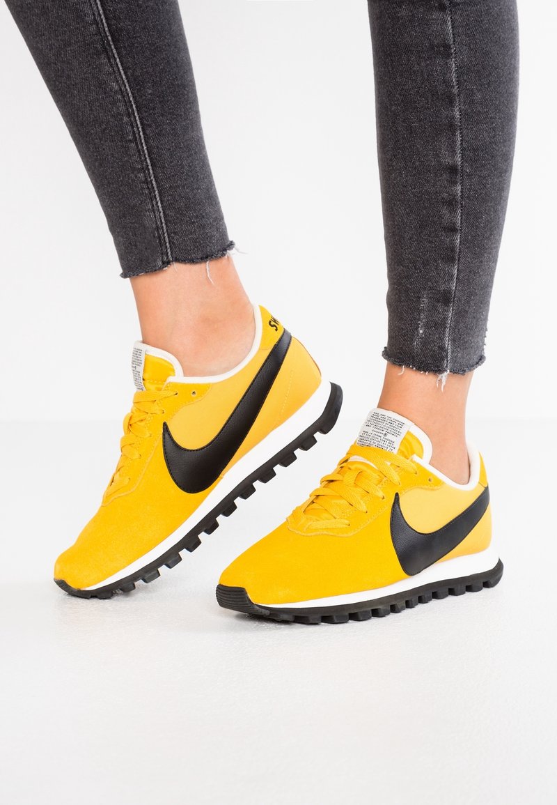 Gula Nike-sneakers med svart swoosh, med en texturerad ovandel, vita detaljer och en svart gummisula med greppklackar.