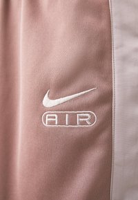 Růžová sportovní látka s bílou vyšívanou logem Nike a bílým nápisem "AIR". Texturovaný povrch s vertikálním žebrováním.