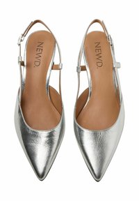 Srebrne metaliczne buty typu slingback z ostrym noskiem o gładkiej fakturze, brązowa skórzana wkładka i regulowany pasek na kostkę. Widoczne logo marki "NEWD".