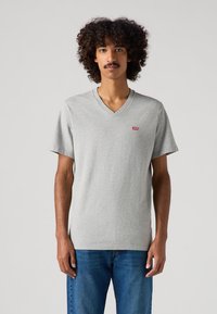 Siva V-majica iz bombaža s kratkimi rokavi, ki ima majhen rdeč logo Levi's na levi prsni strani. Standardna krojena zasnova.