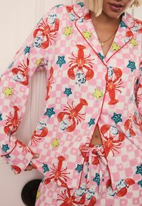 Färgglad rosa pyjamatopp med mönster av hummer, stjärnor och glass, med ett rutigt mönster, knappar och kontrasterande kant.