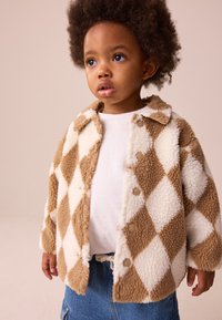 Braun-creme kariertes Fleecepullover mit Kragen, ausgestattet mit Druckknöpfen und einer weichen, strukturierten Oberfläche. Darüber wird ein weißes Hemd getragen.