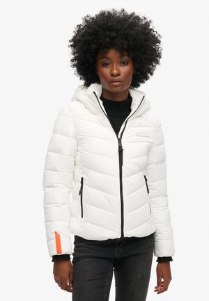 Doudoune blanche avec capuche, présentant un design matelassé, des zips noirs et une touche d'orange sur la manche. Tissu texturé avec une finition lisse.