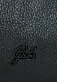 Primo piano di pelle nera con texture, caratterizzato da un logo in rilievo. La superficie presenta un grano distintivo e un aspetto liscio.