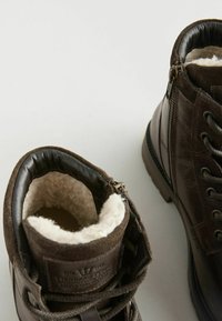 Botas de tobillo de cuero marrón con forro de piel sintética, con cordones en la parte delantera, cremallera lateral y acentos texturizados. Interior suave y liso.