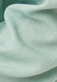 Tissu bleu-vert clair montrant une texture lisse avec de délicates nervures, drapé en douces plis. Le matériau semble léger et flexible.