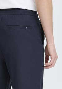 Navy blue pants with a smooth texture, featuring a back pocket and subtle logo accent on the pocket. Elastic waistband for comfort.