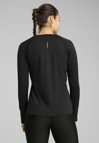 Camiseta deportiva de manga larga en negra, con una tela texturizada, mangas raglán y un pequeño logo reflectante en la parte superior de la espalda.