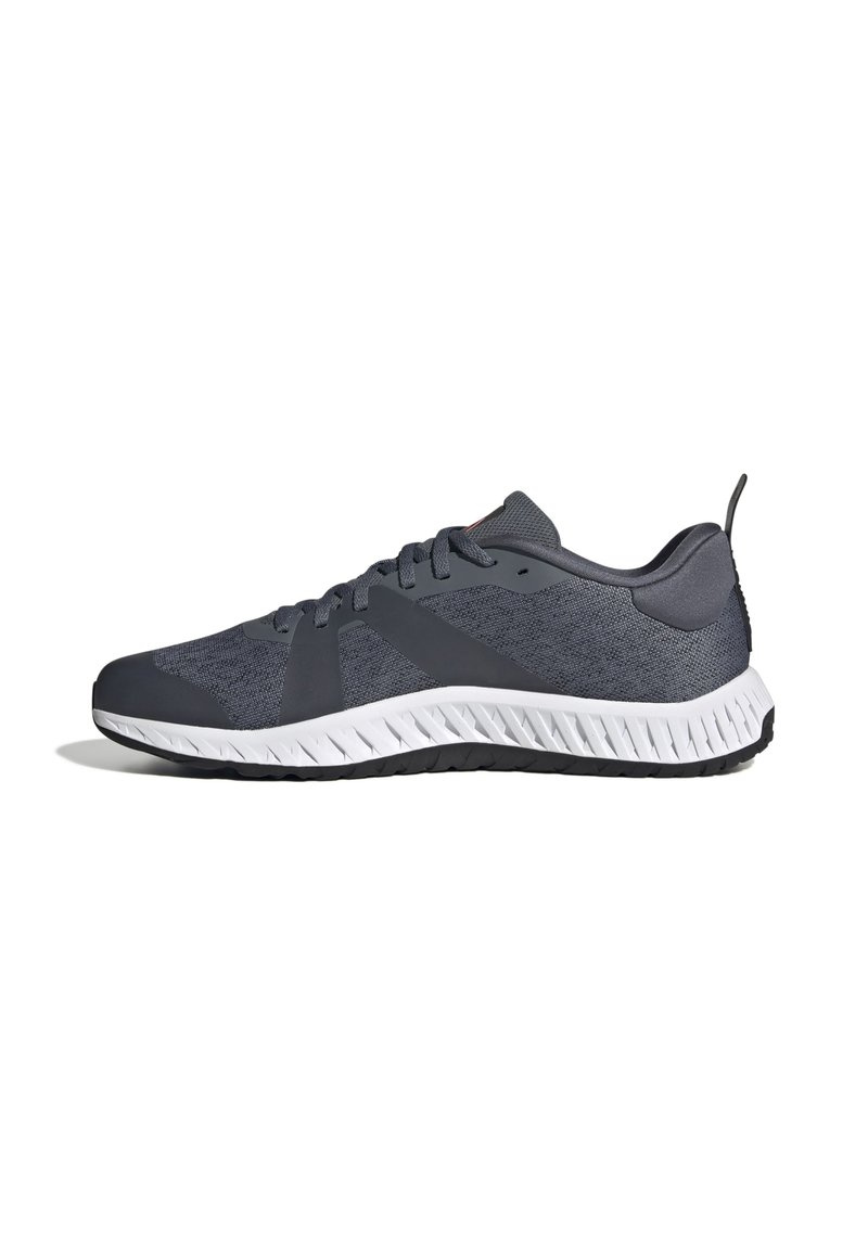Zapatillas deportivas grises con parte superior de tela texturizada, suela de goma contrastante y un diseño aerodinámico. Incluyen cierre con cordones y cuello acolchado.