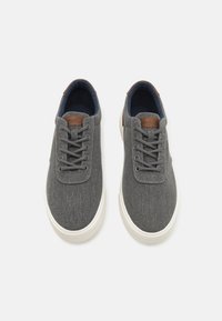 Gray canvas sneakers with a textured finish, featuring gray laces, a brown leather accent on the tongue, and a white rubber sole.