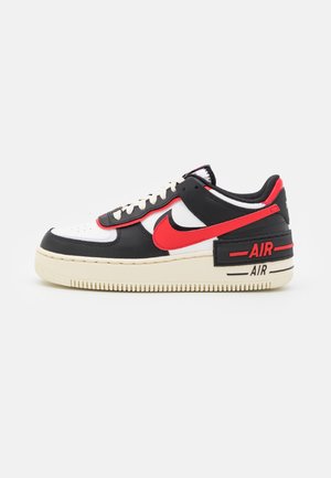 Low-top sneakers in zwart, wit en rood met een rode Nike-swoosh, witte zool en "AIR"-bedrukking op de hiel en zool.