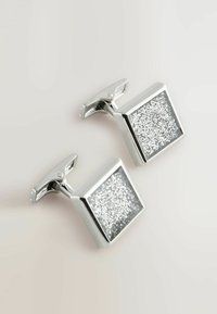 Gemelli in argento di forma quadrata con una superficie texturizzata di particelle di argento incorporate, fissati da una chiusura a cerniera classica.
