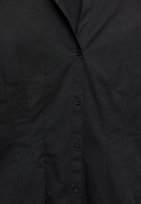 Crna košulja na kopčanje s ovratnikom i okomitim šavovima, s četiri gumba niz sredinu sprijeda.