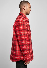 Red and black plaid flannel shirt with long sleeves, button-down closure, and a single chest pocket, displayed on a neutral background.