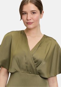 Olivgrünes Wickelkleid mit kurzen, flatternden Ärmeln, strukturiertem Stoff und V-Ausschnitt. Glatte Textur mit dezentem Glanz.