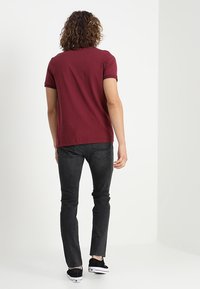 Mörkröd bomullströja med korta ärmar, kombinerad med svarta skinny jeans och svarta sneakers. Enkel bakvy, inga grafik eller mönster.