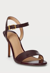 Σκούρο μπορντό λουστρίνι σάνδαλο με ψηλό τακούνι, λουράκι στον αστράγαλο, χρυσό κούμπωμα και ανοιχτή μύτη, σε λευκό φόντο.