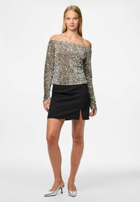 Sānu atklātais sudraba sekvīnu topiņš, kombinēts ar pieguļošu melnu mini svārku ar sānu izgriezumu. Modelis rotā sudraba papēžu kurpes.