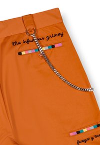 Pantalones de tela naranja con detalle de cadena. Presentan texto bordado y acentos a rayas coloridas en los bolsillos. Textura suave y diseño moderno.