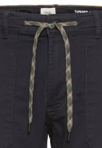 Marineblå tapered bukser med et camo-mønster, snor i metal, og et syet waistband-label. Stoffet ser glat og holdbart ud.