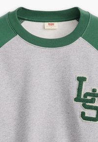 Sweat-shirt gris avec manches raglan vertes, un logo texturé en vert et blanc, et un tissu doux en mélange de coton. L'étiquette indique "Levi's".